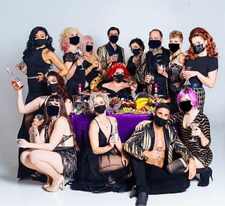 Pictured is the whole group of the Corsets & Cuties holding champagne glasses while wearing black masks. 